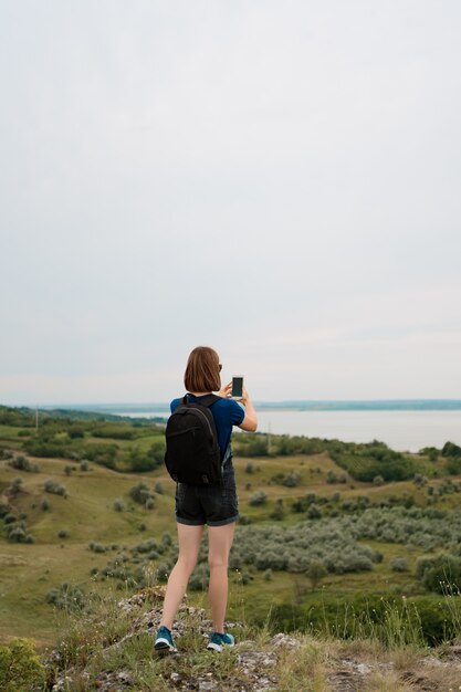 Woman hiker taking photo with smart phone at hill peak.