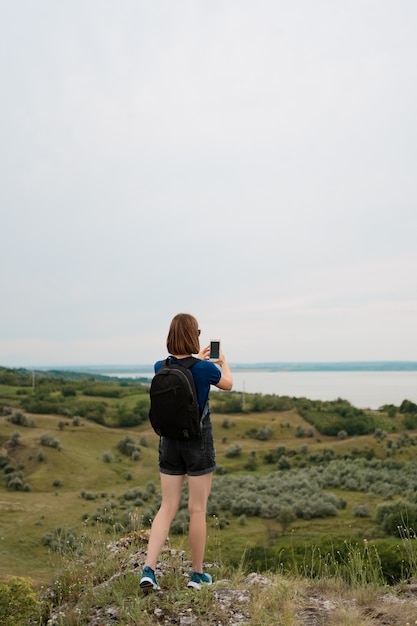 女性ハイカーは丘の頂上でスマートフォンで写真を撮影。