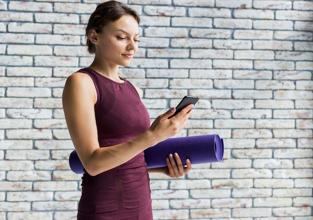 Женщина держит коврик для йоги, стоя на своем телефоне