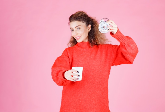 Free photo woman holding an alarm clock and a cup of coffee pointing at her morning routine.