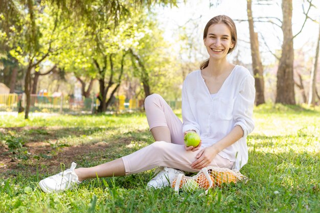 草の上に座っているリンゴを保持している女性