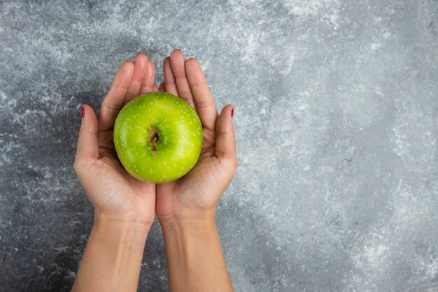 Woman holding apple with both hands on marble.