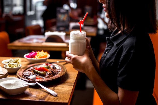 Woman holding ayran mug served with iskender kebab