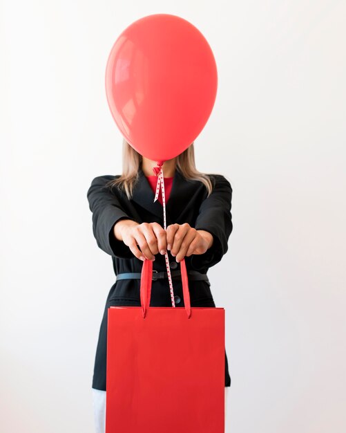 Woman holding bag and red balloon covering her face