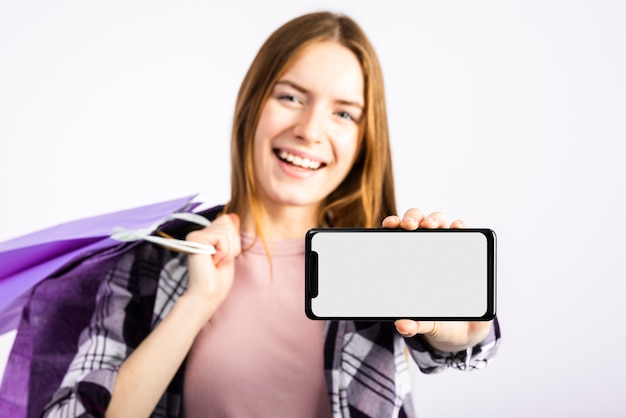 Woman holding bags and showing phone at camera