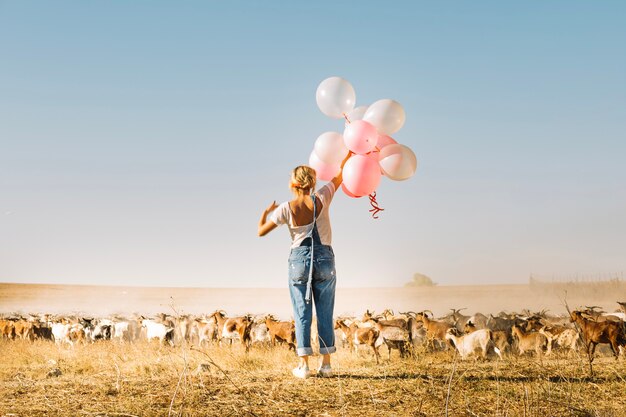 Woman holding balloons near goat herd