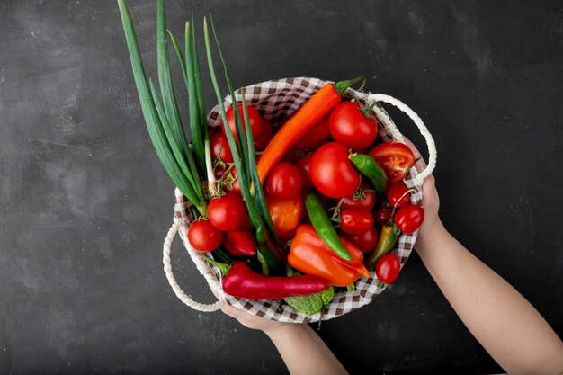 Woman holding basket of tomatoes peppers and scallions on black surface