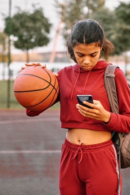 彼女の電話をチェックしながらバスケットボールを保持している女性