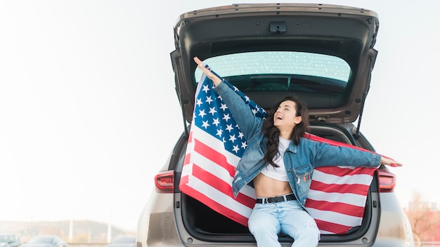 Woman holding big usa flag in car trunk