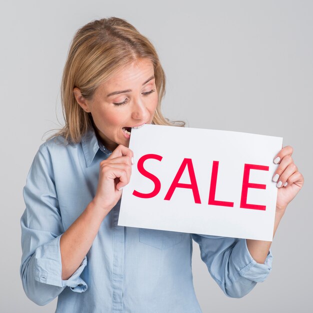 Woman holding and biting from sale sign
