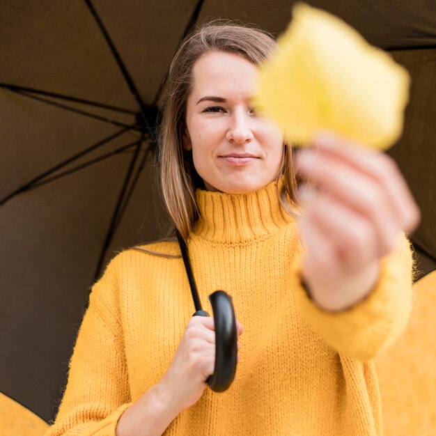 Женщина, держащая черный зонт и желтый лист
