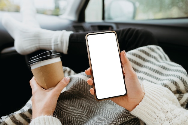 空白の電話と一杯のコーヒーを持っている女性