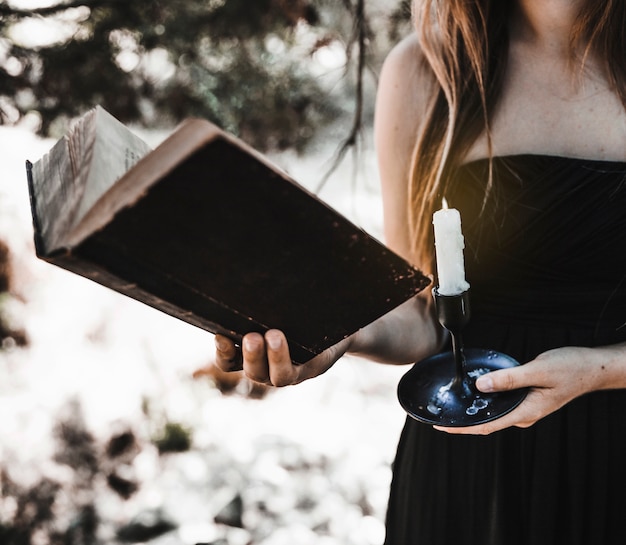 Woman holding book and candle in forest