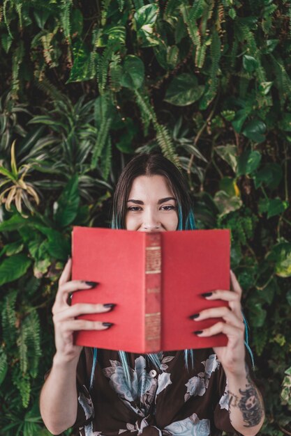 Woman holding book in front of her mouth standing against plant