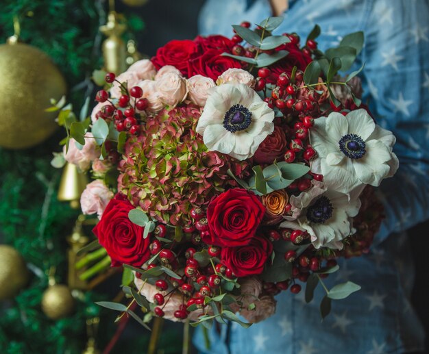 A woman holding a bouquet of autumn colour flowers in the hand on a christmas decoration wall backgorund.