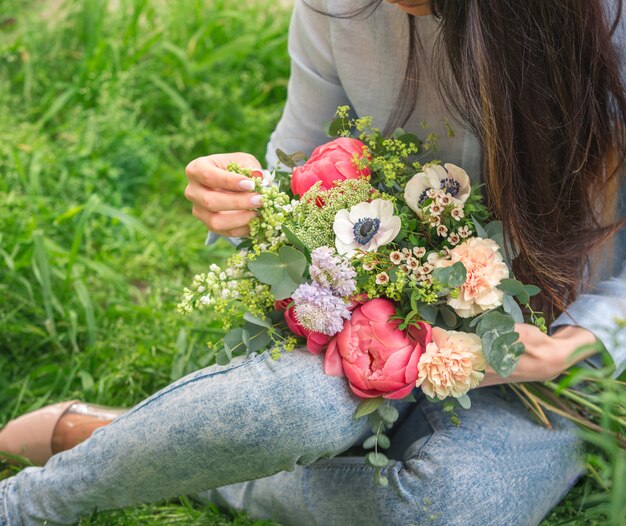 手に色とりどりの花の花束を保持し、緑の草の上に座っている女性