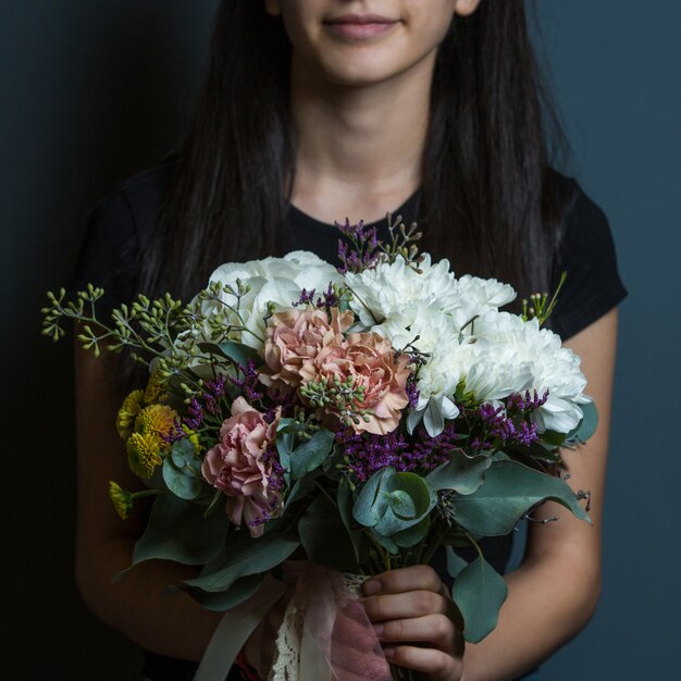 A woman holding a bouquet of colorful, mostly white peonies in the hand on a room wall backgorund.