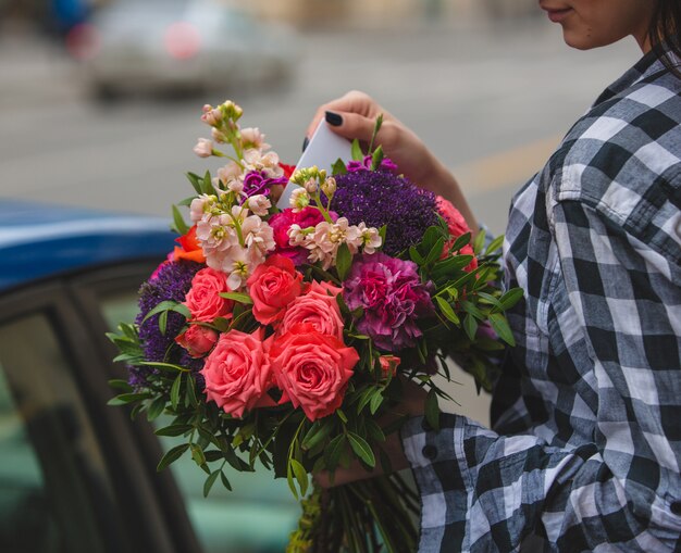 A woman holding a bouquet of colorful roses and taking the greeting card in the hand on street 