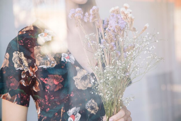 Woman holding bouquet of dry plants behind window