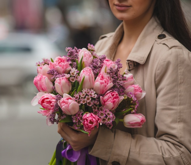 Женщина держит в руке букет из розовых тюльпанов и сирен