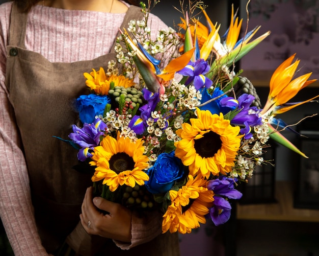 Free photo woman holding bouquet of sunflowers iris and blue rose
