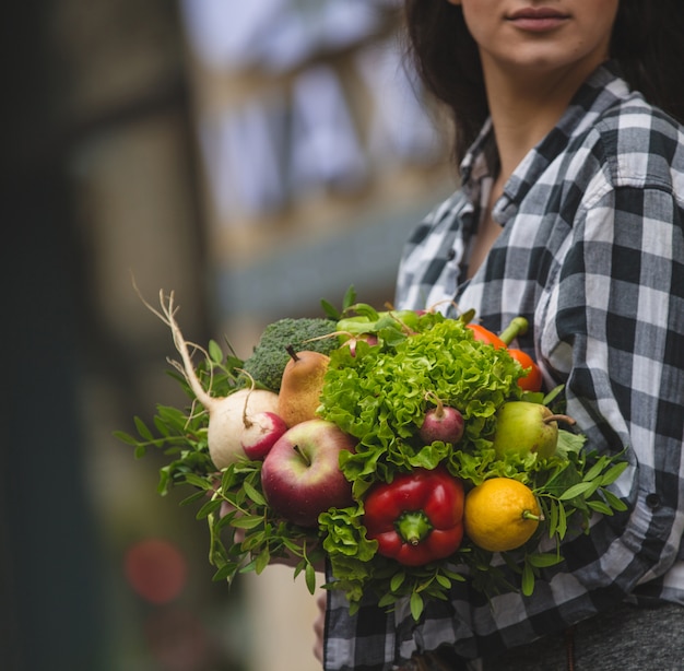 A woman holding a bouquet of vegetables and fruits in the hand on street 