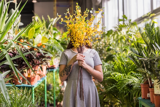 緑の植物間の顔の近くの小枝の束を保持している女性