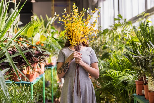 Woman holding bunch of twigs near face between green plants