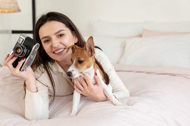 Woman holding camera and dog in bed