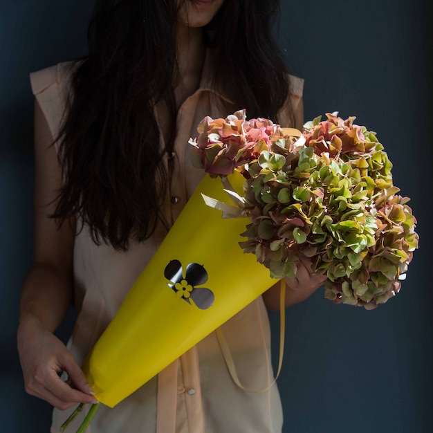 Free photo a woman holding a cardboard bouquet of yellow leaf flowers in the hand on a room wall