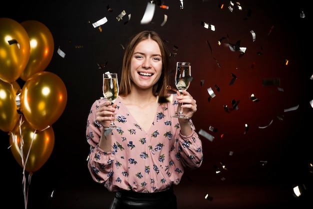 Woman holding champagne glasses surrounded by confetti and balloons