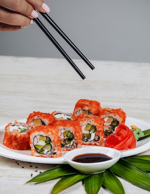 Free photo woman holding chopsticks to take sushi rolls with red tobiko