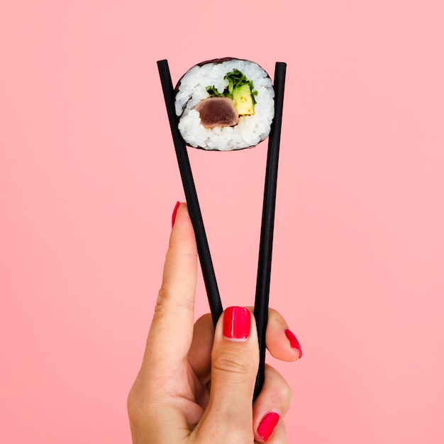 Woman holding chopsticks with sushi roll