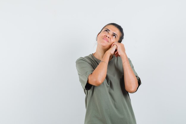 woman holding clasped hands on cheek in t-shirt and looking dreamy