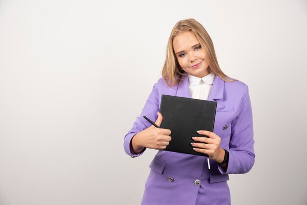 Woman holding clipboard on white wall. 