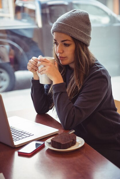 여자가 커피 컵을 들고 레스토랑에서 노트북을보고