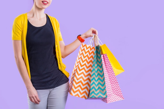 Woman holding colorful paper shopping bag against purple wallpaper