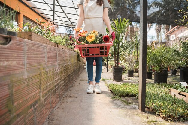 Woman holding container of colorful flowers in greenhouse