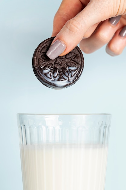 Woman holding a cookie above glass of fresh milk