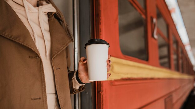 電車の横にコーヒーを持っている女性