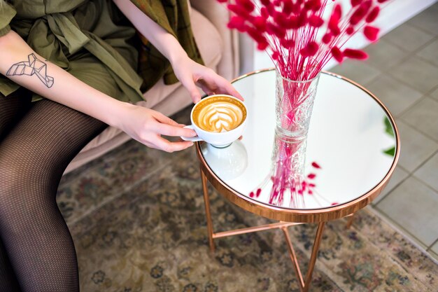 おいしいカプチーノのカップを保持している女性とレストラン、派手な雰囲気、コーヒー愛好家での時間をお楽しみください。