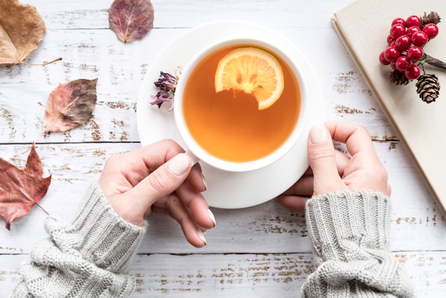 葉の間でお茶のカップを保持している女性