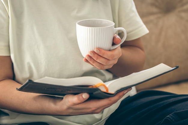 woman-holding-cup-tea-reading-book-sofa-home-close-up_169016-48843.jpg
