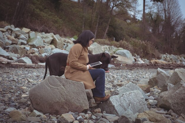 Женщина, держащая цифровой планшет собакой на пляже