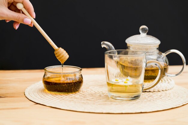 Woman holding dipper over honey jar near glass and teapot