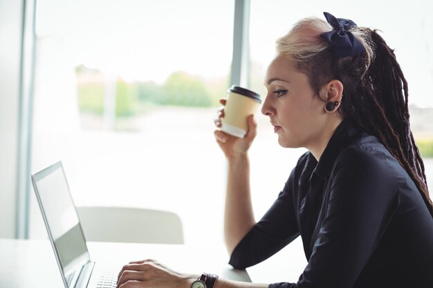 Woman holding disposable coffee cup while using laptop