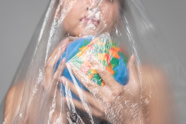 Woman holding an earth globe while being covered in plastic close-up