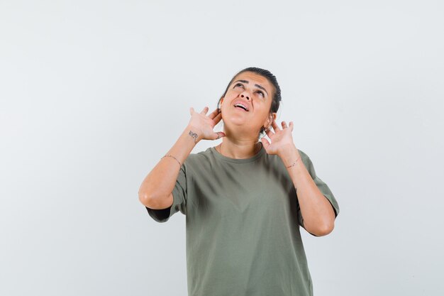 woman holding fingers behind ears in t-shirt and looking curious