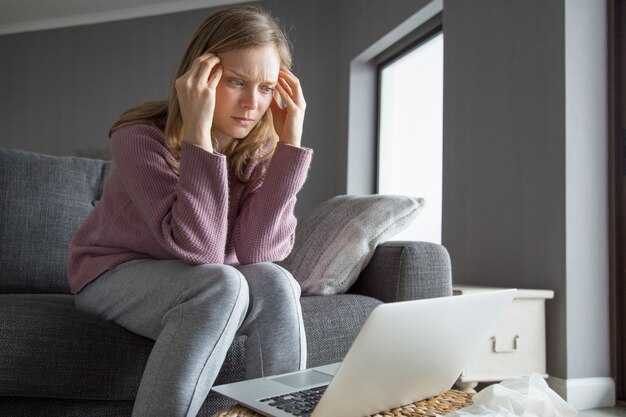 Woman holding fingers on temples, looking at laptop on table