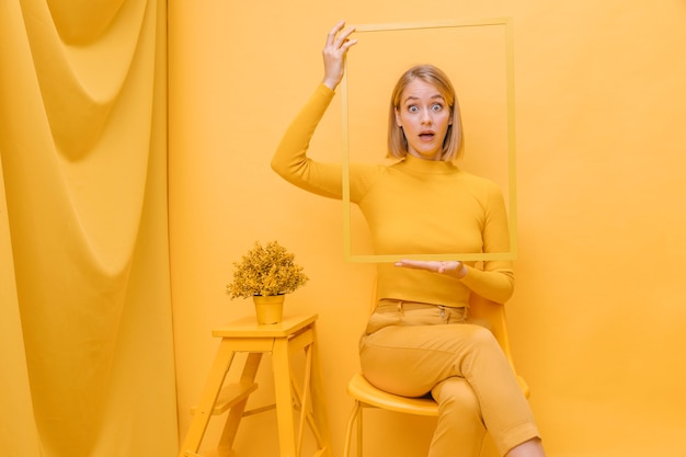 Бесплатное фото Женщина держит рамку вокруг лица в желтой сцене